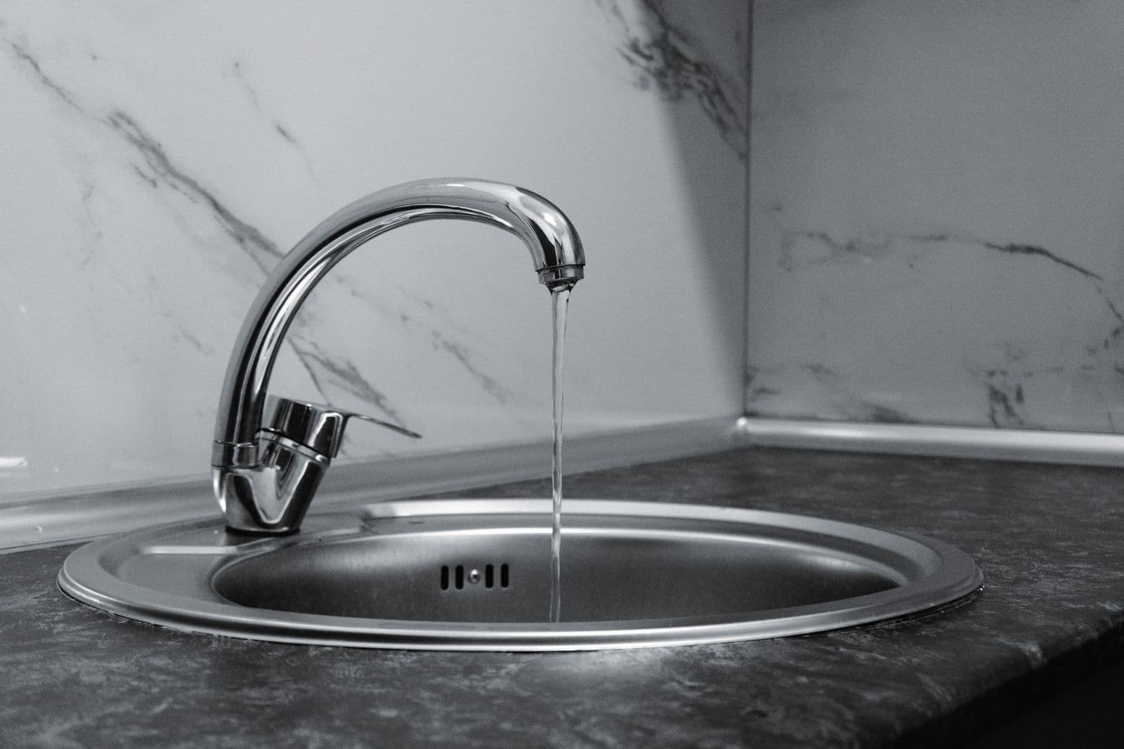 Chrome kitchen faucet with water running onto a marble counter