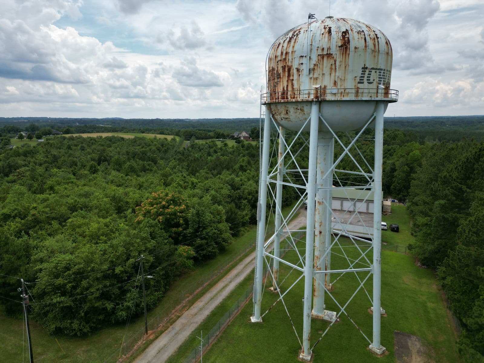 Aerial view of a rusted water tower standing in green fields