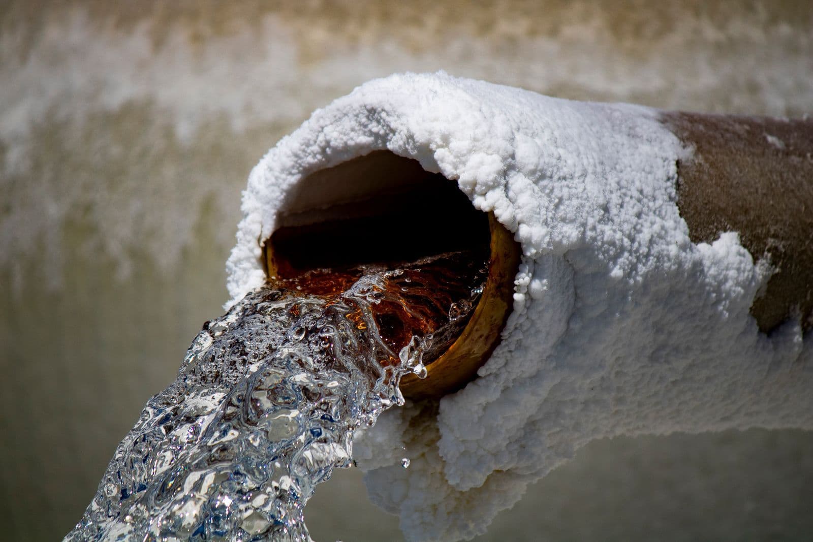 Water flowing from a rusty pipe crusted with mineral deposits