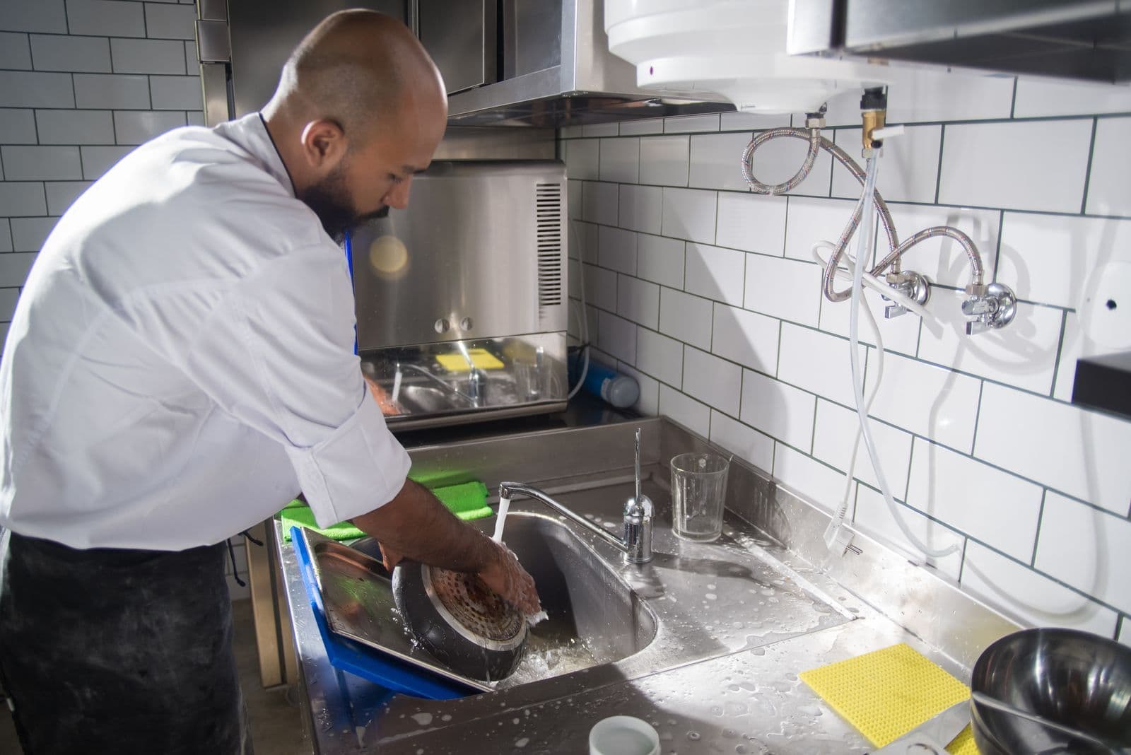 Chef cleaning kitchen utensils at a stainless steel sink